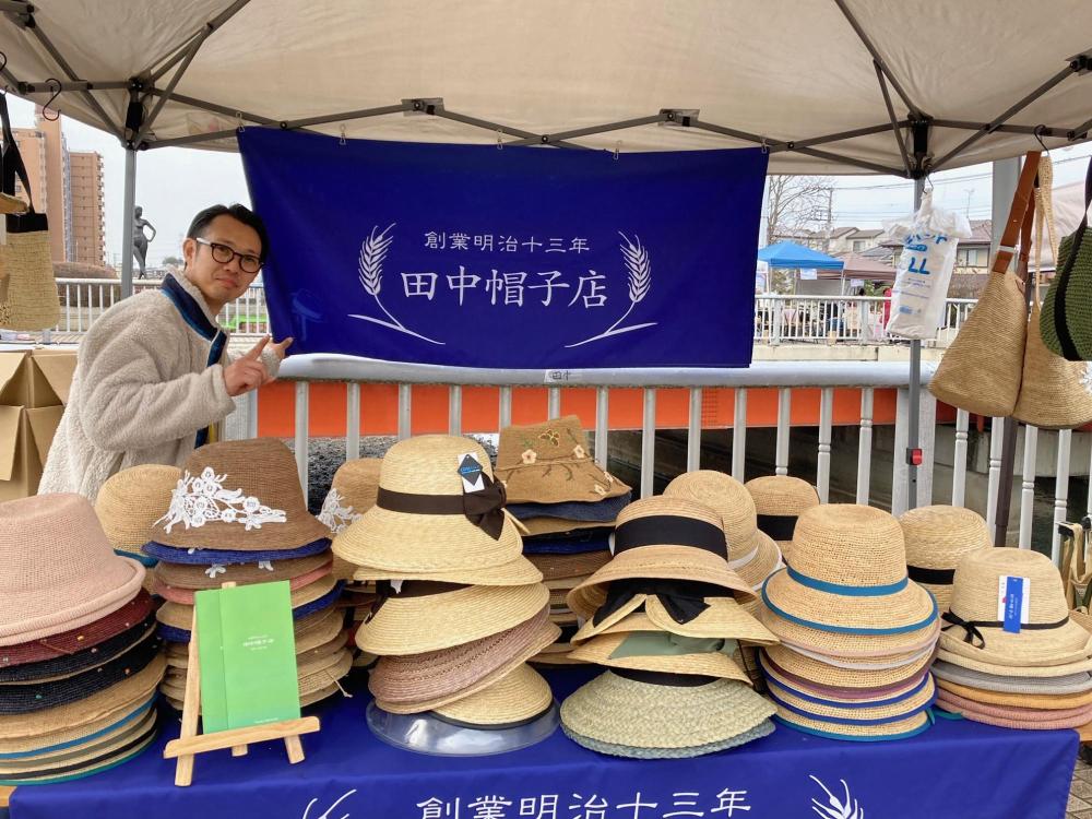 お店の旗を手にポーズをきめる田中帽子店の田中さん