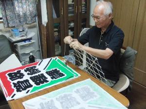 白髪の男性が、凧の枠組みを組み立てている写真