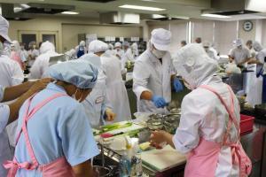 エプロンを着けてキャップを被った女性数名が調理をしている写真