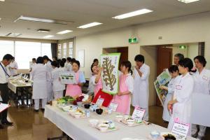 室内で献立が並ぶテーブルを前に発表をしている人たちの写真