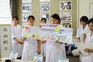 自由献立と書かれた題目と、イラストや文字が書かれた紙を手に発表を行う人たちの写真