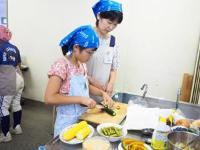 青い三角巾をつけた親子がまな板で具材を切っている写真