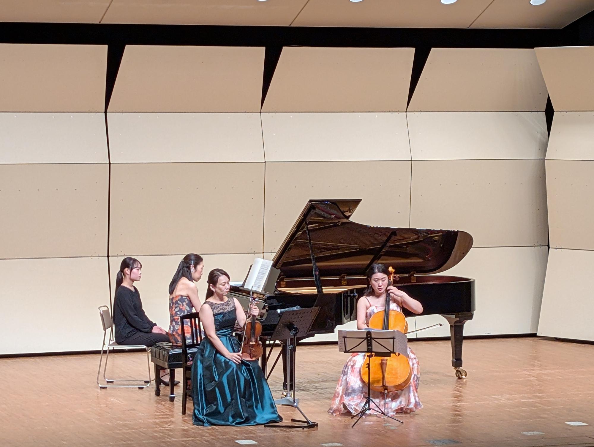 ステージ上でチェロとヴァイオリンとピアノを演奏する様子