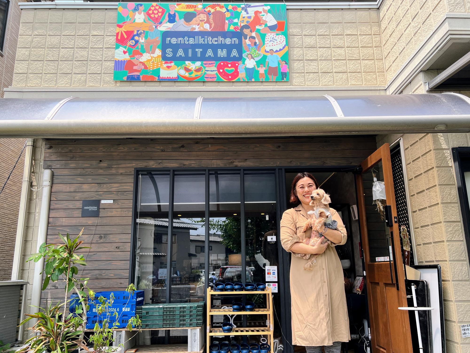 レンタルキッチンSAITAMAの店舗前で愛犬を抱き微笑むおおさとさん