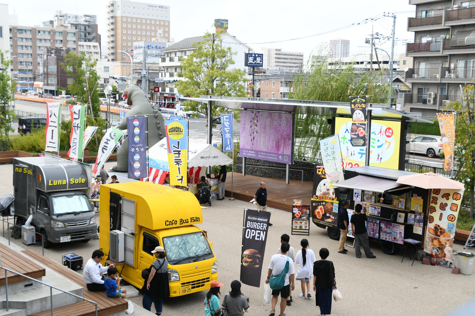 キッチンカーやテントが並ぶ「まちなかひろば」を本庁舎2階から写した写真。複数の来場者がキッチンカーのメニューを見たり、買ったものを食べたりしている。