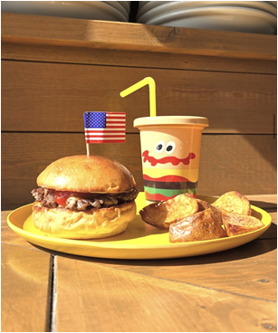アメリカの国旗が刺さった小さいチーズバーガーと、フライドポテト、ハンバーガーの絵柄が描かれたドリンクボトルが並ぶ、キッズプレートの写真