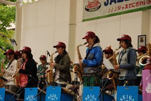 赤いキャップをかぶった人たちが、並んで吹奏楽器を演奏している写真