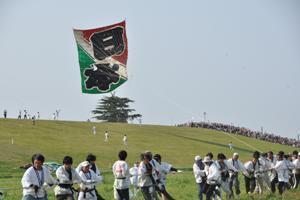 多くの人が協力して、日本と書かれた大きな凧をあげている写真