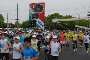 春日部と書かれた大きな凧を掲げて、多くの人がマラソンをしている写真