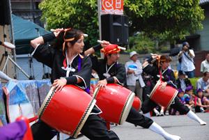 赤い太鼓を腰にくくりつけて、バチを振り下ろそうとしている人たちの写真