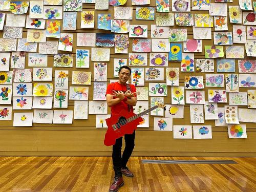 かすかべ親善大使のはなわさんが粕壁小学校の児童が描いた絵の前で埼玉ポーズをする様子