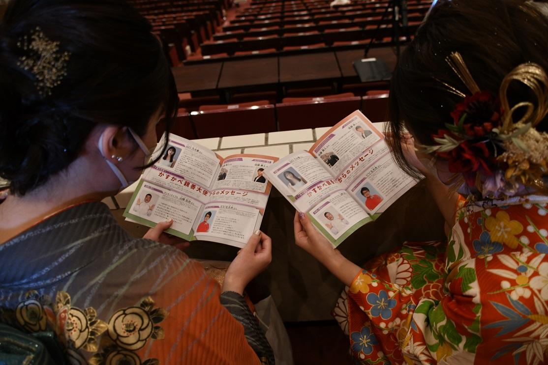 二十歳を祝う会記念しに掲載された春日部親善大使からのメッセージを読む式典参加者の様子