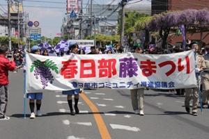 春日部藤まつりと書かれた横断幕を持って道を歩く人たちの写真