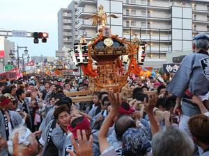 はっぴを着た大勢の人たちが、金色のみこしを担ぎあげている写真