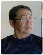 紺色のシャツを着て、左を向いている関根隆さんの写真