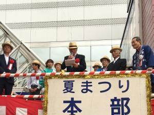 紅白の櫓の前であいさつをしている男性の写真