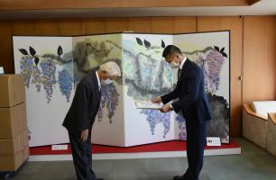 藤が描かれた屏風の前で向かい合い、内山さんへ感謝状を贈呈している写真