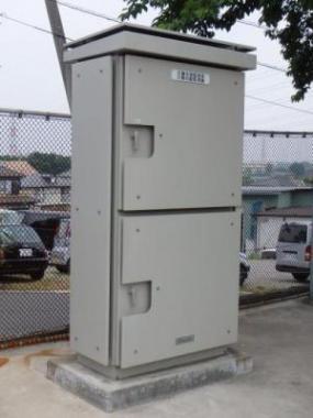 金網の前に設置されたコンクリートの基礎上に建てられた水道水の水質や水圧を測定する末端監視装置の写真