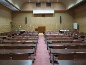 長机と椅子が並び、奥には演台がある大会議室の写真