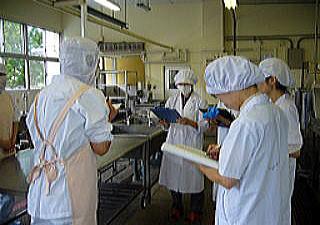 学校給食室の施設で衛生指導を行う栄養士たちの写真