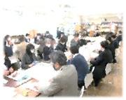 長く並べられた机に多数の人が座っている写真