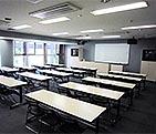 たくさんの机が並べられ、正面に大きな白いスクリーンがある視聴覚研修室の写真