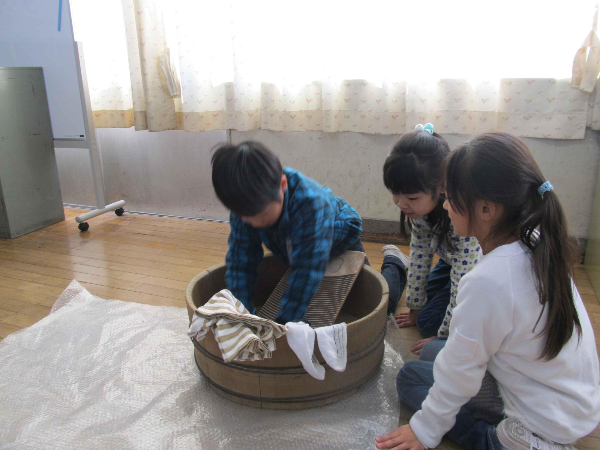 洗い桶と洗濯板で、昔の洗濯体験をする児童たちの写真