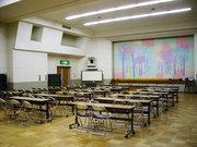 ステージにパステル調のイラストのスクリーンがかけられている武里大枝公民館講堂机といすを置いた状態）の写真